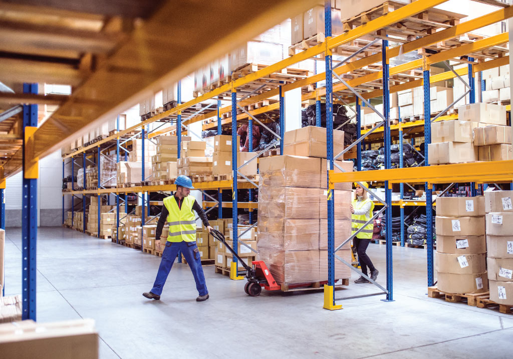 Warehouse workers moving palletized boxes with a pallet jack inside a large distribution warehouse with industrial storage racks.